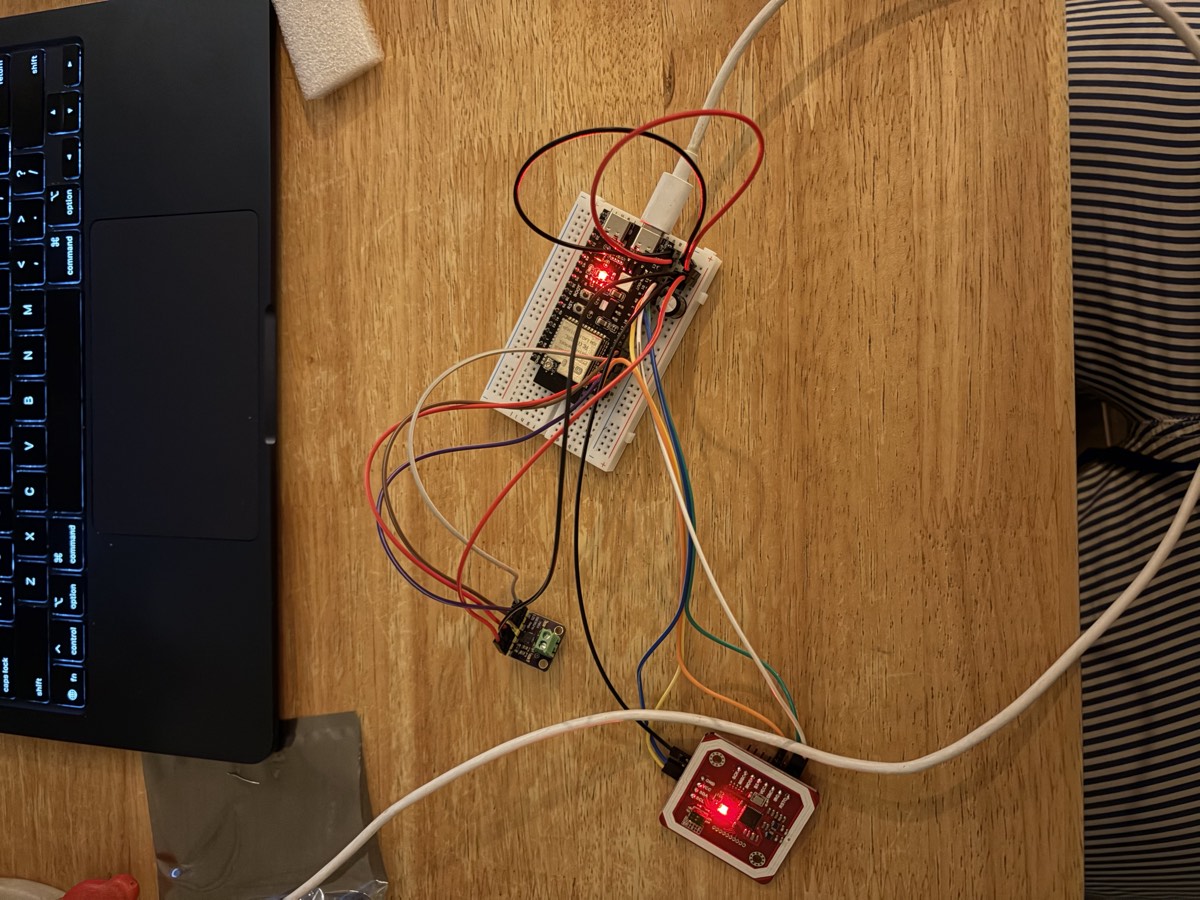 Un ESP32 enfiché sur une breadboard blanche, relié par une dizaine de fils de couleur à un lecteur NFC rouge dont la LED est allumée.
