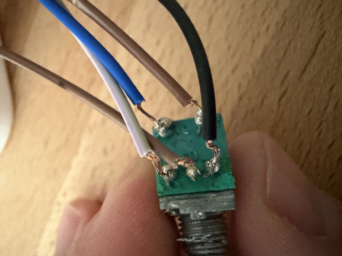 Un potentiomètre tenu entre deux doigts, cinq fils de couleur soudés à ses cosses.